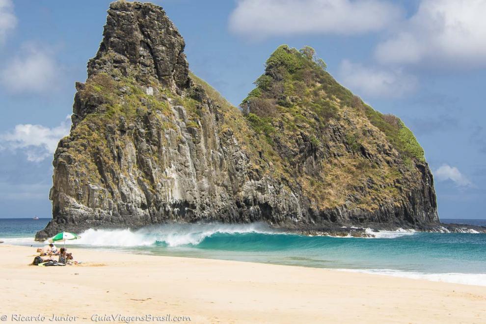 Imagem de turistas nas areias e ondas na beira da Praia Cacimba do Padre.